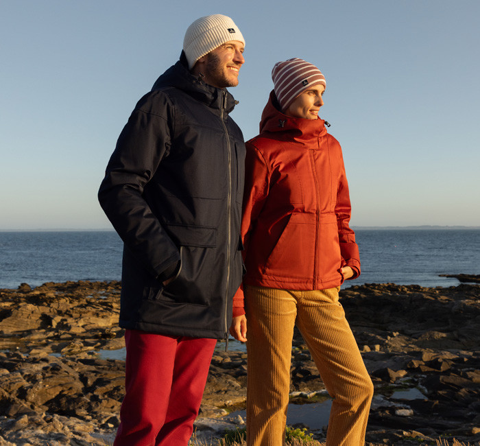 Un homme et une femme au bord de mer portant des parkas et bonnets Mousqueton