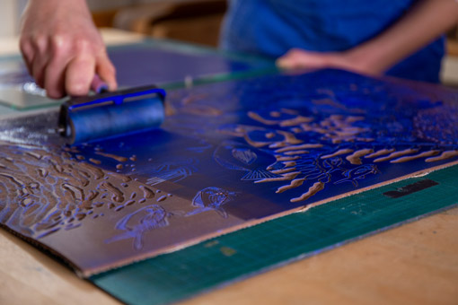 Morgane Chouin en train de passer un rouleau d'encre bleue sur sa linogravure Mousqueton