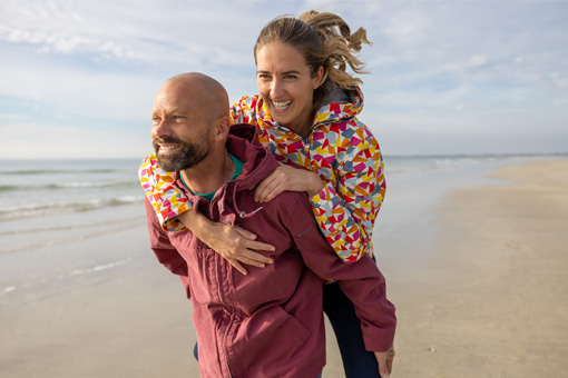 Un homme et une femme se promenant au bord de mer avec leurs vestes en toile Mousqueton