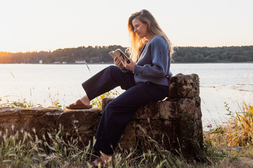 Femme portant un gilet en maille 100% laine au bord de l'eau avec un livre