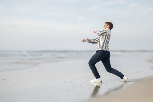 Homme qui fait des ricochets en bord de mer avec un pull marin