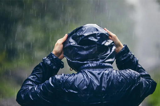 Homme de dos sous la pluie avec une veste imperméable noire à capuche